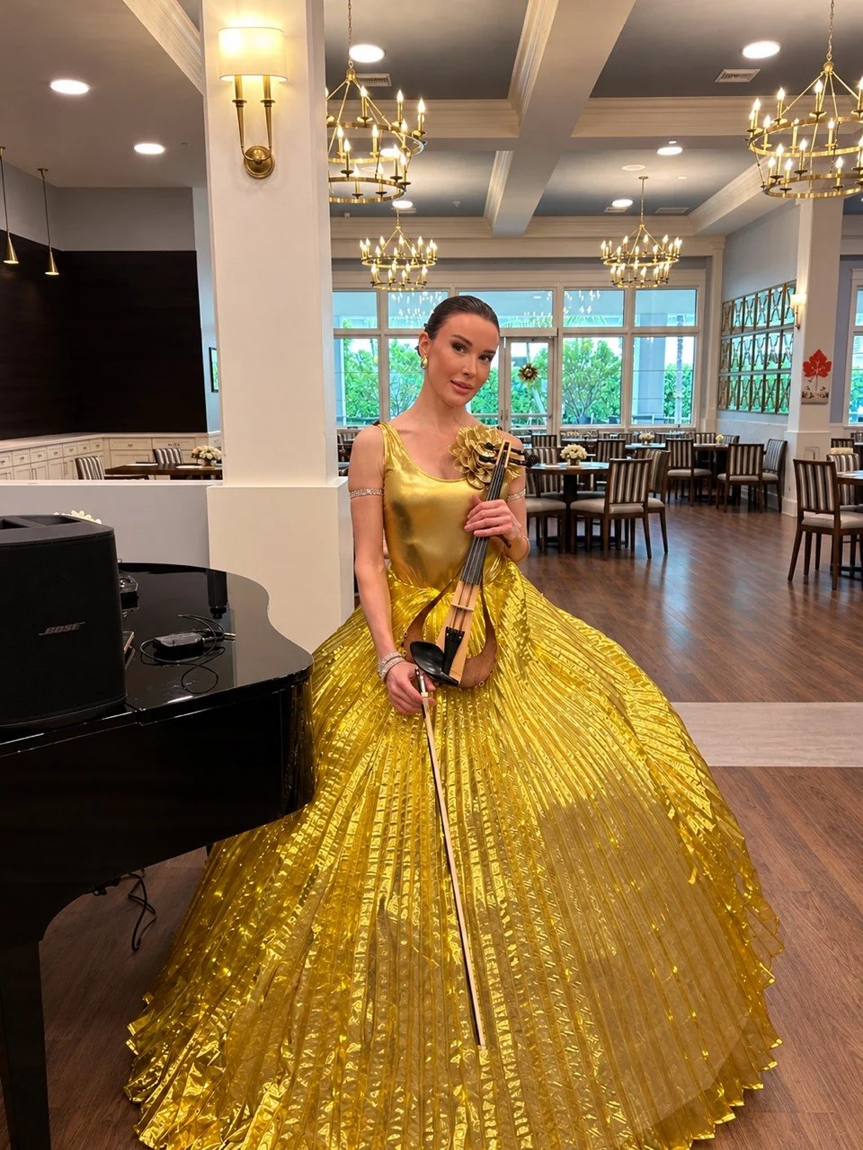 Anna Cordin with an electric violin in a gold gown beside a grand piano