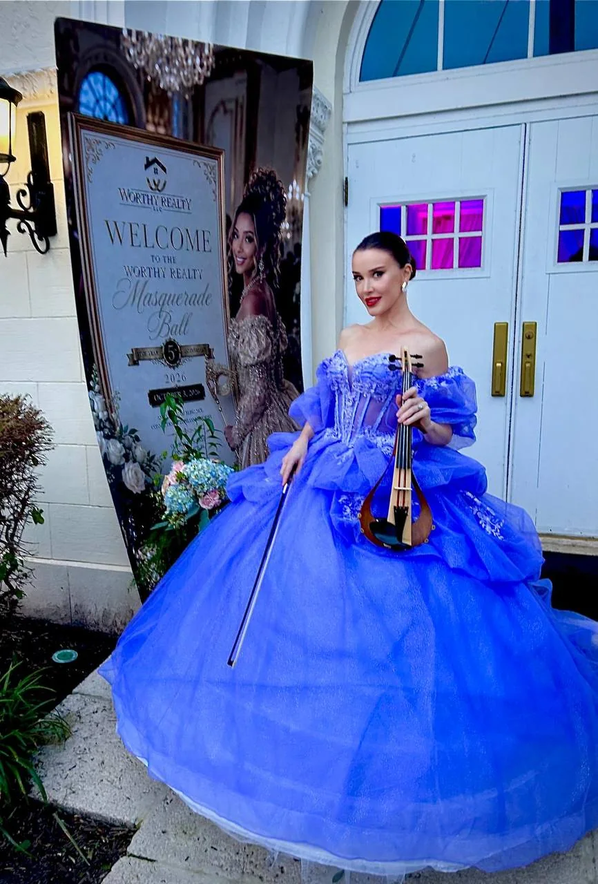 Anna Cordin holding her violin in a blue-lavender ball gown at an event entrance
