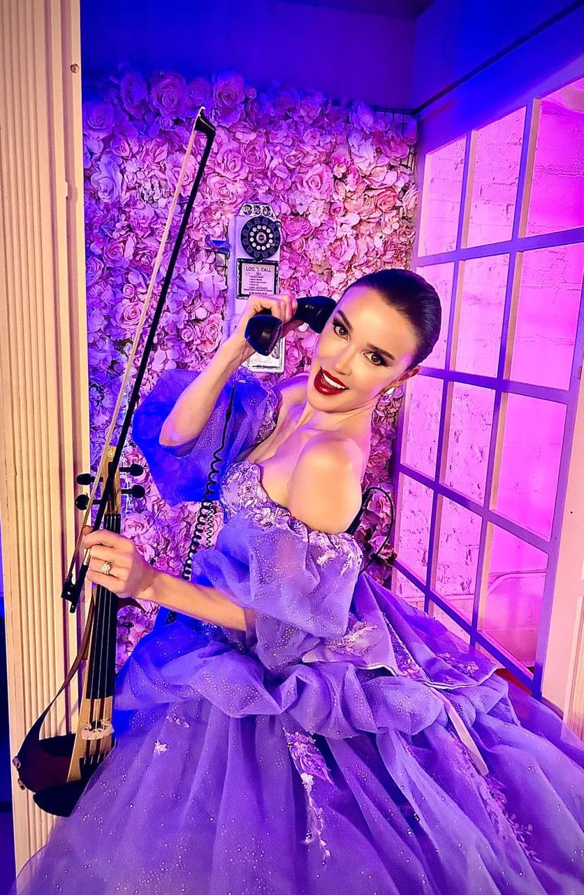 Anna Cordin with her violin and a telephone receiver in a lavender gown