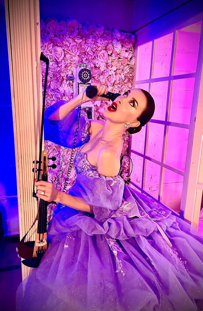 Anna Cordin with her violin and a telephone receiver in a flower-lined booth
